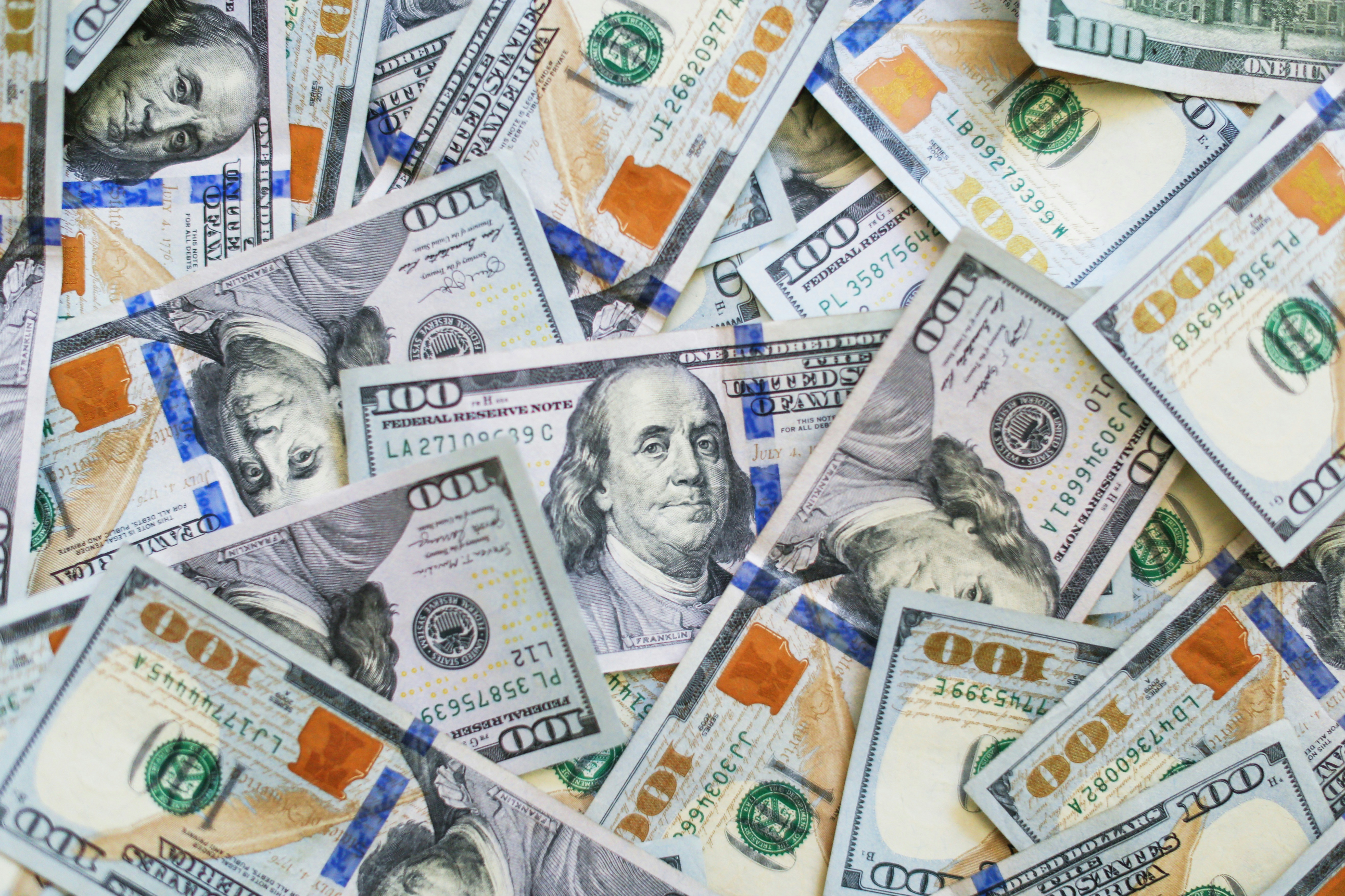 Scattered U.S. hundred-dollar bills with Benjamin Franklin's portrait visible on multiple notes.